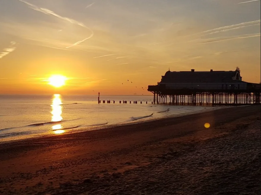 Cleethorpes pier at sunset, low tide, sun reflecting off the wet sand.